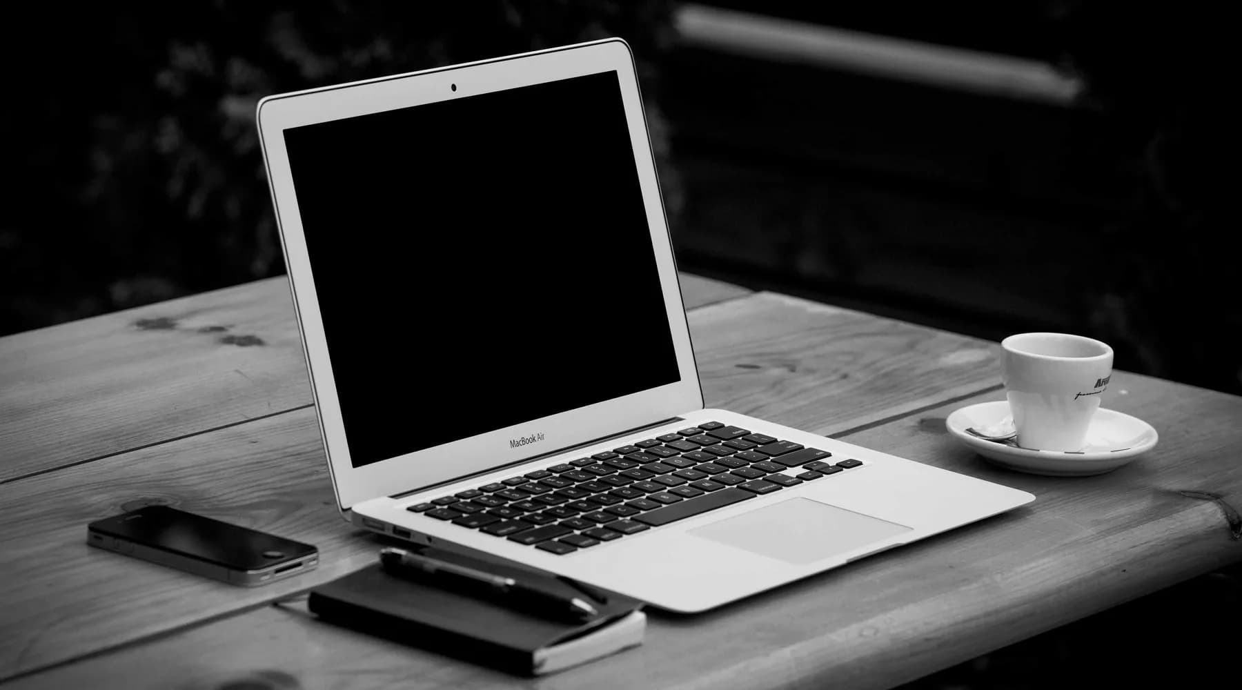 Ordinateur portable, carnet et tasse posés sur un bureau en bois.